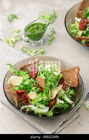 Salad with frisee lettuce, sun dried tomatoes, cheese, bread chips and pesto dressing Stock Photo