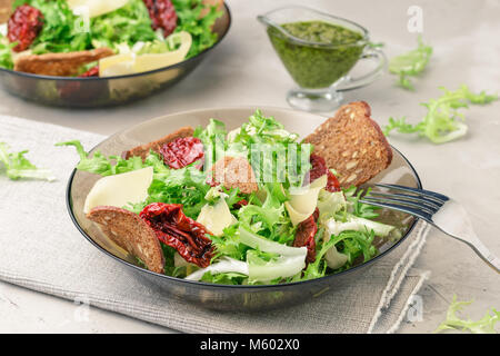 Salad with frisee lettuce, sun dried tomatoes, cheese, bread chips and pesto dressing Stock Photo