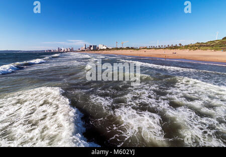 Coastal landscape close up waves breaking on beach against blue city skyline in Durban, South Africa Stock Photo