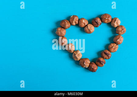 Filbert nuts, lay out in the form of heart on a bright blue painted wooden background. Stock Photo