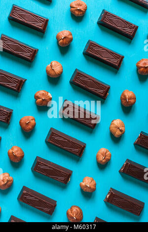 Top view a rhythmical flat lay set of rectangular pieces of chocolate and hazelnuts on blue wooden background.