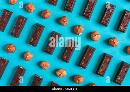Flat lay geometric pattern of pieces of chocolate and hazelnuts on blue wooden background. Stock Photo