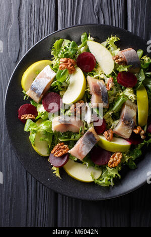 Freshly prepared mackerel salad with apples, walnuts, beets and mix lettuce close-up on a black plate on the table. Vertical top view from above Stock Photo