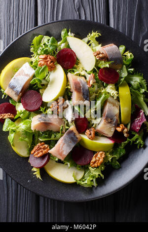 Fresh mackerel salad with apples, walnuts, beets and mix lettuce close-up on a plate on the table. Vertical top view from above Stock Photo