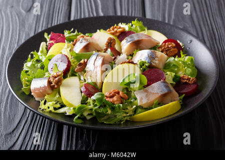 Gourmet salad with mackerel with apples, walnut, beetroot and mix lettuce close-up on a black plate on the table. horizontal Stock Photo