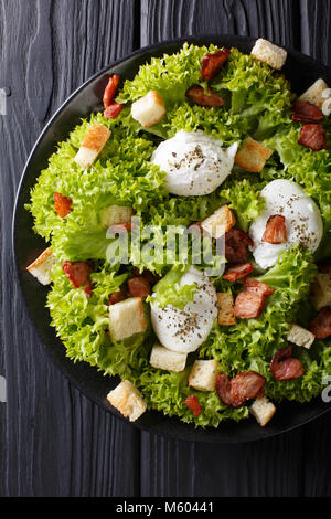 Organic French Lyonnaise salad with lettuce, bacon, croutons and poached eggs close-up on a plate on the table. Vertical top view from above