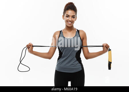 Sport, training, lifestyle and Fitness concept - portrait of beautiful happy African American woman exercising with jumping rope. Isolated on white studio background. Stock Photo