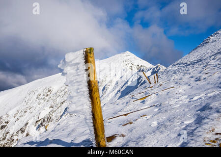 Wind blown ice on fence post with view to Snowdon peak from Rhyd Ddu path below Bwlch Main in winter snow in Snowdonia National Park. Wales UK Britain Stock Photo