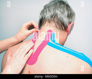 female physiotherapist applies tape on back of caucasian man Stock Photo