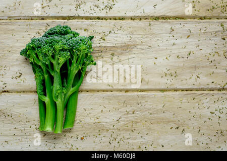 high angle view of some stems of broccolini on an off-white rustic wooden surface with some blank space on the right Stock Photo
