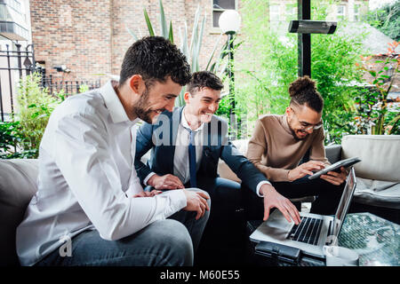 Businessmen are working together on wireless technology in a business meeting taking place in a bar courtyard. Stock Photo
