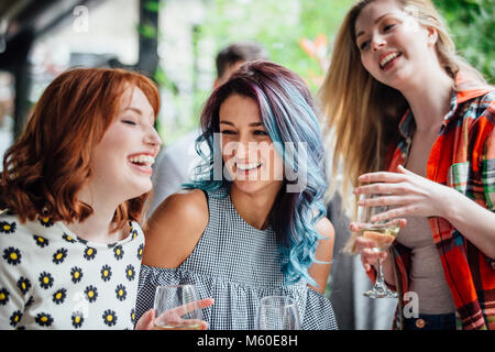 Three women are talking while enjoying drinks in a bar courtyard. They are laughing and drinking wine. Stock Photo