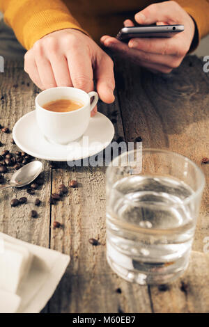 Man drink coffee while using a smartphone, glass of water and newspaper on table. Stock Photo