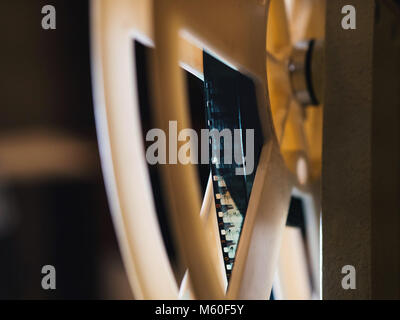 Front view of an old-fashioned antique Super 8mm film projector, projecting a beam of light in a dark room next to a stack of unraveled film reels. Stock Photo