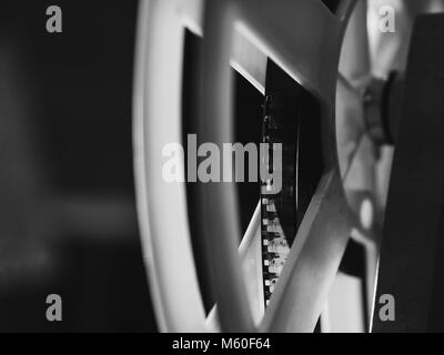 Front view of an old-fashioned antique Super 8mm film projector, projecting a beam of light in a dark room next to a stack of unraveled film reels. Stock Photo