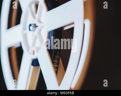 Front view of an old-fashioned antique Super 8mm film projector, projecting a beam of light in a dark room next to a stack of unraveled film reels. Stock Photo