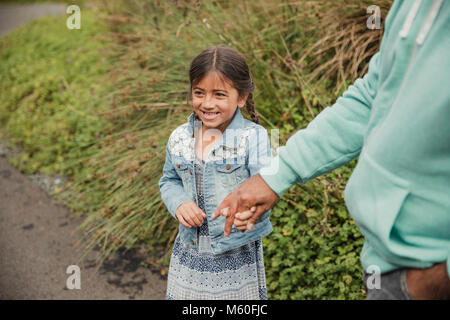 Little girl standing outside, laughing and holding her fathers hand. Stock Photo