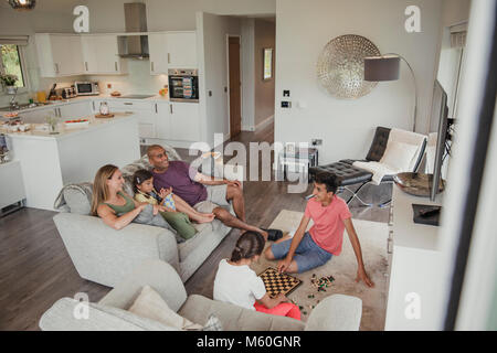 Family relaxing in their holiday home. Two of the children are playing chess while the rest of the family watch. Stock Photo