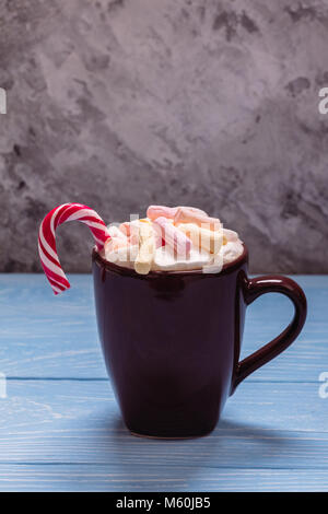 A cup full of marshmallow and a New Year's candy in it on a blue table and on a gray background Stock Photo