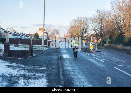 A man rides his bike in the wintry cold conditions in February 2018, wearing a fluorescent jacket and back pack. Stock Photo