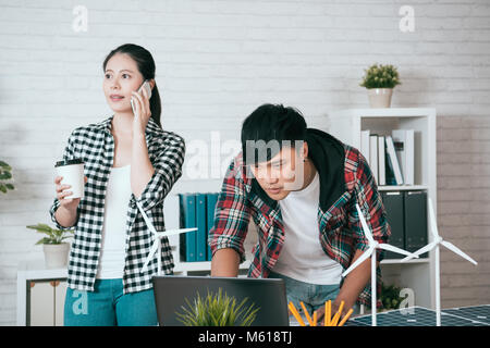 beautiful female alternative energy engineer talking on the phone call and male engineer using computer to check the price detail for their customer c Stock Photo