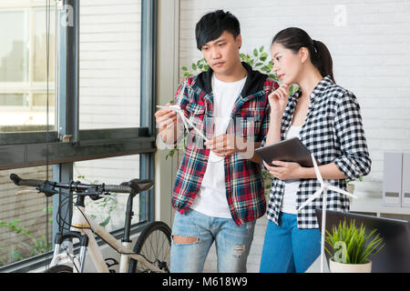 male alternative energy engineer holding a windmill sample and discuss with his female engineer colleague together standing by window in the studio Stock Photo