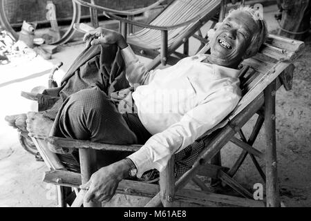 Bagan, Myanmar, December 27, 2017:  Senior man recovers in an armchair and smokes a cigarette Stock Photo