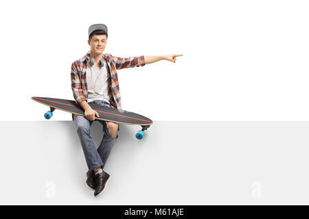 Teenage skater with a longboard sitting on a panel and pointing isolated on white background Stock Photo