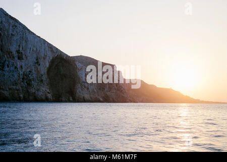 Bright sun setting over rocky cliffs and calm surface of sea.