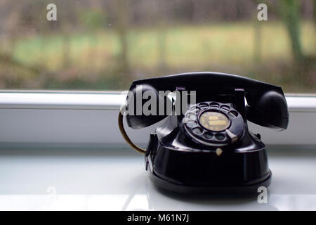 Vintage black telephone on the table near window with blurred background. Stock Photo