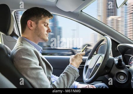 Side View Of A Young Man Sitting Inside Car Using Mobile Phone Stock Photo
