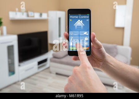 Close-up Of A Human Hand Holding Mobile Phone With Home Control System On Screen Stock Photo