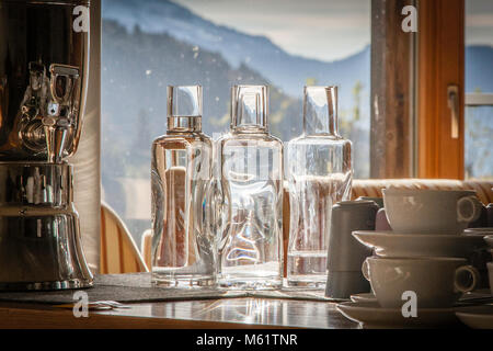 Elmauer Water - mountain spring water -three bottles of spring water standing in front of a window with mountains in the background. Elmau water - a scientifically backed drinking water. The best mountain spring water flows in the ship from all drinking water fittings. Before that, it passes through the Ellmauer Light and Energy Generator to compensate for energy and light deficiencies in the water molecules Stock Photo