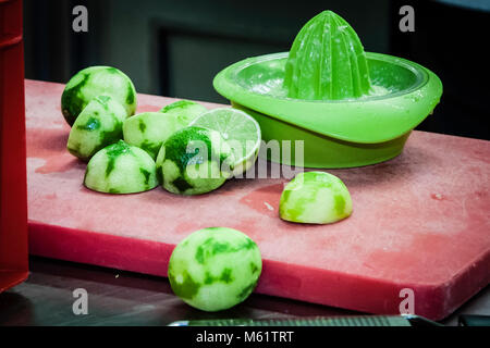 A green plastic citrus reamer for squeezing limes stands on a red cutting board in the kitchen of the Ambassador Hotel & Spa in Sankt Peter-Ording, Germany. Several halved and squeezed limes lie beside it, their peels dark green in patches. Star chef Marco Müller uses the juice and zest of the limes to season a dish at the Schleswig-Holstein Gourmet Festival. Stock Photo