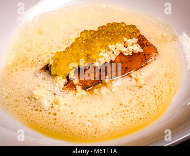 Fillet and caviar of char with cauliflower, tofu and mace is a course served by German two-star chef Michael Kempf at the gourmet evening at the Parkhotel Ahrensburg, Germany. A red-toned fish fillet sits beneath golden caviar pearls and white crumbs in a frothy yellow butter sauce. Kempf is head chef of Berlin's two-Michelin-star restaurant Facil at Hotel Mandala. Stock Photo
