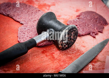 Raw venison cutlets are flattened with a meat mallet before being breaded in the Jagdhaus kitchen of the Romantik Hotel Freiberg in Oberstdorf, Bavaria, Germany. A hand then spreads mustard onto one of the flattened cutlets. Stock Photo