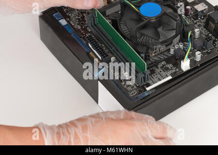 Close up of man hands with gloves installing Ram DDR4 memory module in slot on motherboard.