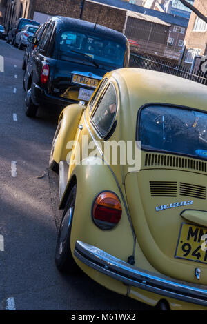 A Volkswagen Beetle original yellow coloured car next to a black cab london taxi in a back street in the capital. Original yellow vw beetle car iconic Stock Photo