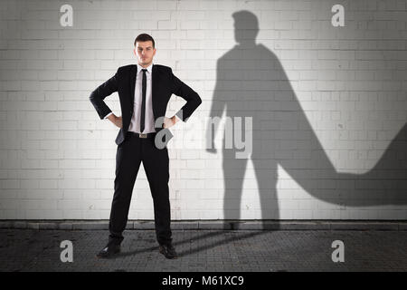 Shadow Of Superhero Formed On Wall Behind The Young Businessman Stock Photo