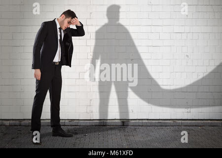 Young Tired Businessman With His Own Shadow In Superhero Cape Stock Photo