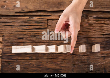 High Angle View Of Person's Hand Stopping Dominoes Continue Toppled At Wooden Desk Stock Photo