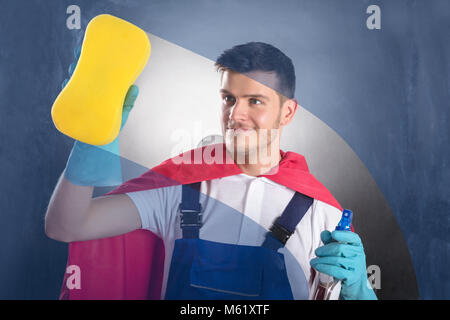 Young Happy Male Janitor In Red Cape Cleaning Glass Stock Photo