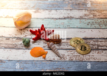 Two golden bitcoins with seashells and starfish on vintage wooden table Stock Photo