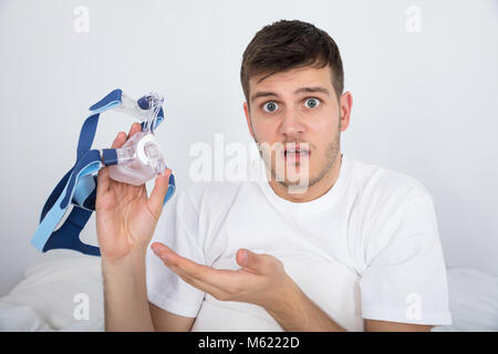 Close-up Of Shocked Young Man Holding CPAP Machine Mask Stock Photo
