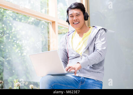 Chinese young man wearing casual clothes while using a laptop Stock Photo