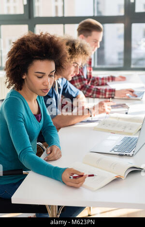 Close-up on student holding a pen over a book while studying Stock Photo