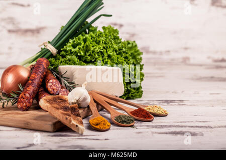 Smoked very delicious sausage with rosemary, cheese, toast and spices in spoons on a wooden rustic background. Top view. Stock Photo