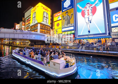 Osaka, Japan - April 29, 2017: touristic boat in Dotonbori Canal and famous Glico Running Man sign in Dotonbori street, Namba, a popular shopping and entertainment district. Nightlife and night scene. Stock Photo