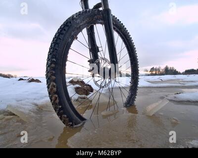 Winter mtb riding in snowy country. Low ankle view to wheel with snow mud tyre. Melting of snow flakes in tyre tread pattern. Stock Photo
