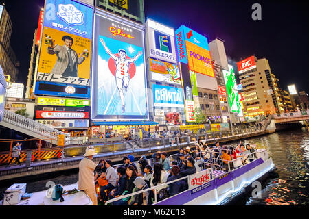 Osaka, Japan - April 29, 2017: touristic boat in the Dotonbori Canal with neon lights of the Glico Running Man sign in Dotonbori street, Namba, a popular shopping and entertainment district. Stock Photo